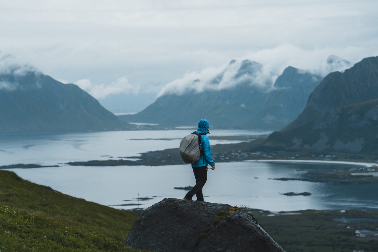 Hiker on misty mountain peak in rain gear, with vast sea view.