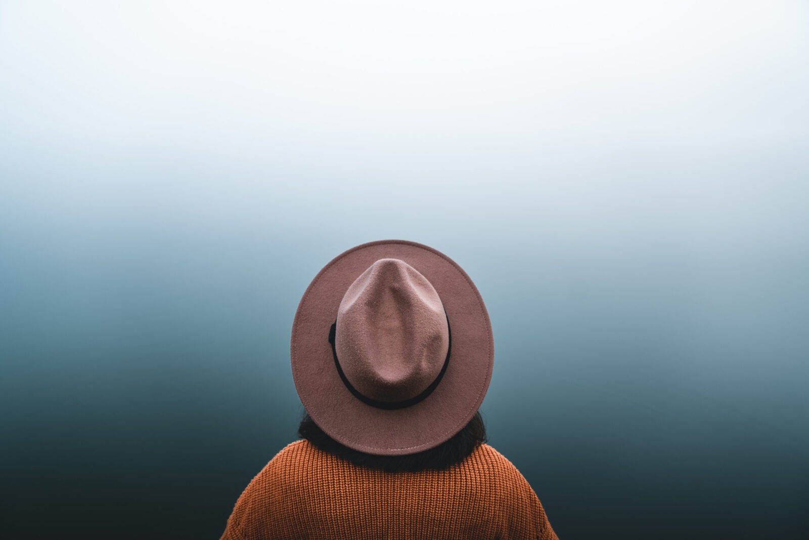 Close-up of person's back with fedora hat and textured sweater.