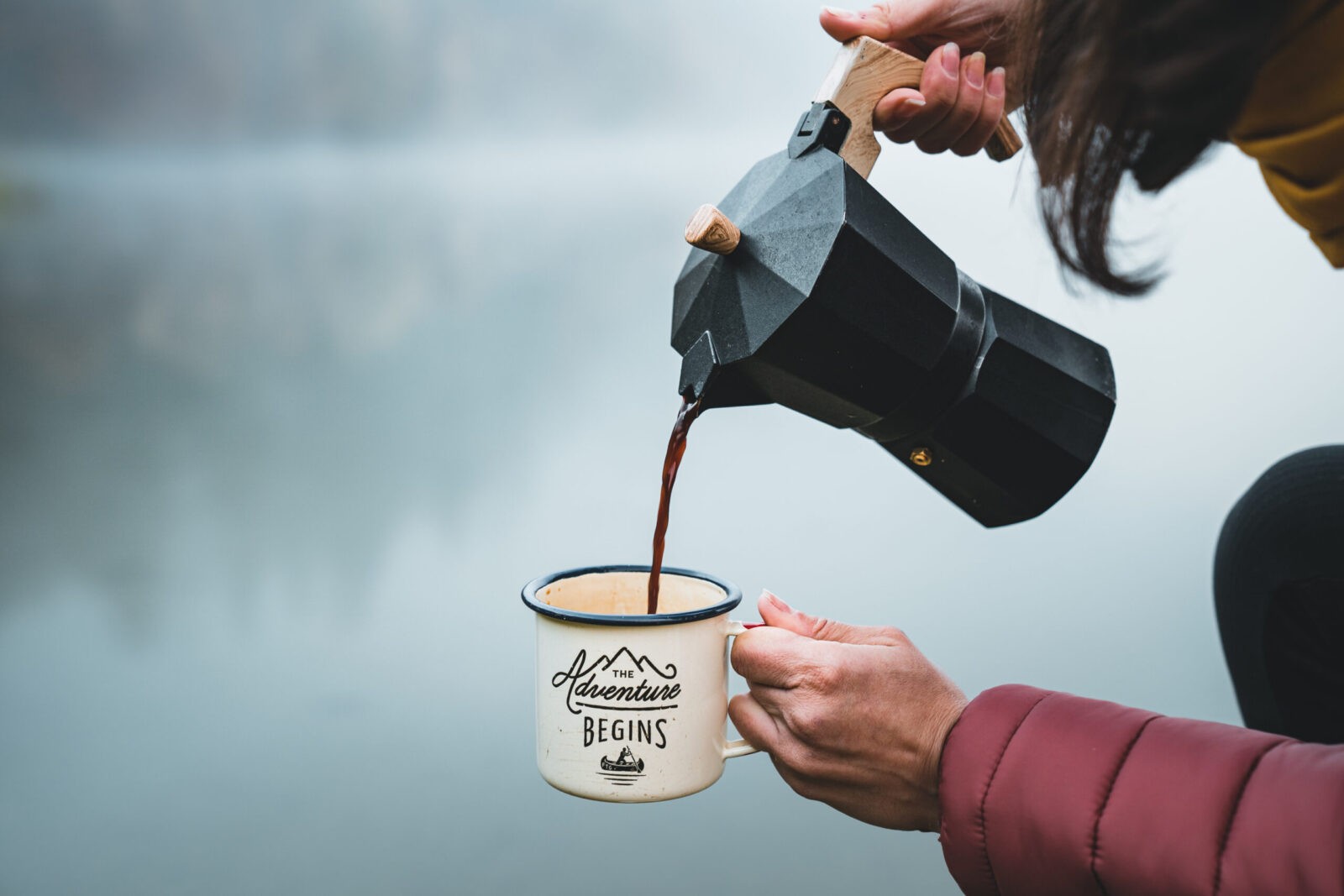 Close-up of Moka pot pouring coffee into "The Adventure Begins" mug.