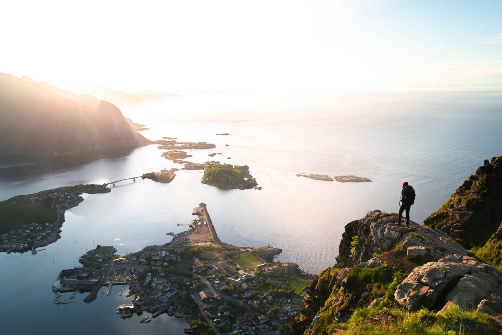 Experience the breathtaking beauty of Reinebringen, Lofoten, Norway. A hiker admires the stunning panorama of fjords, mountains, and the vast ocean.